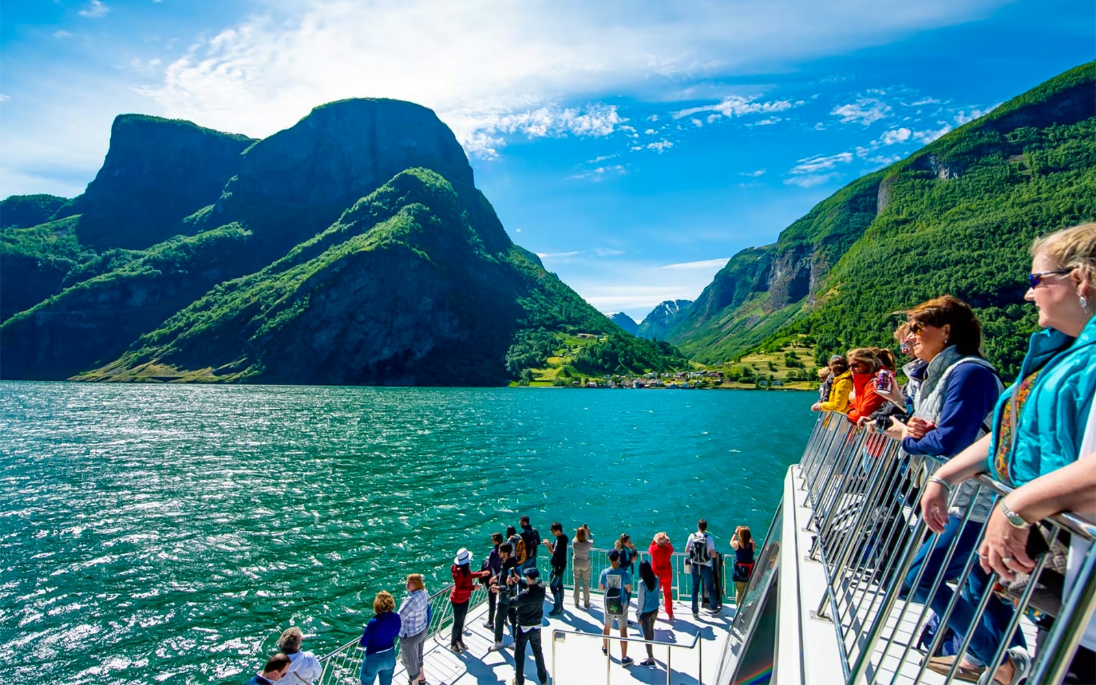 Tourists on a cruise ship deck enjoying views of Nærøyfjord's mountains and water.