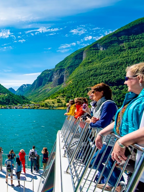 Tourists on a cruise ship deck enjoying views of Nærøyfjord's mountains and water.