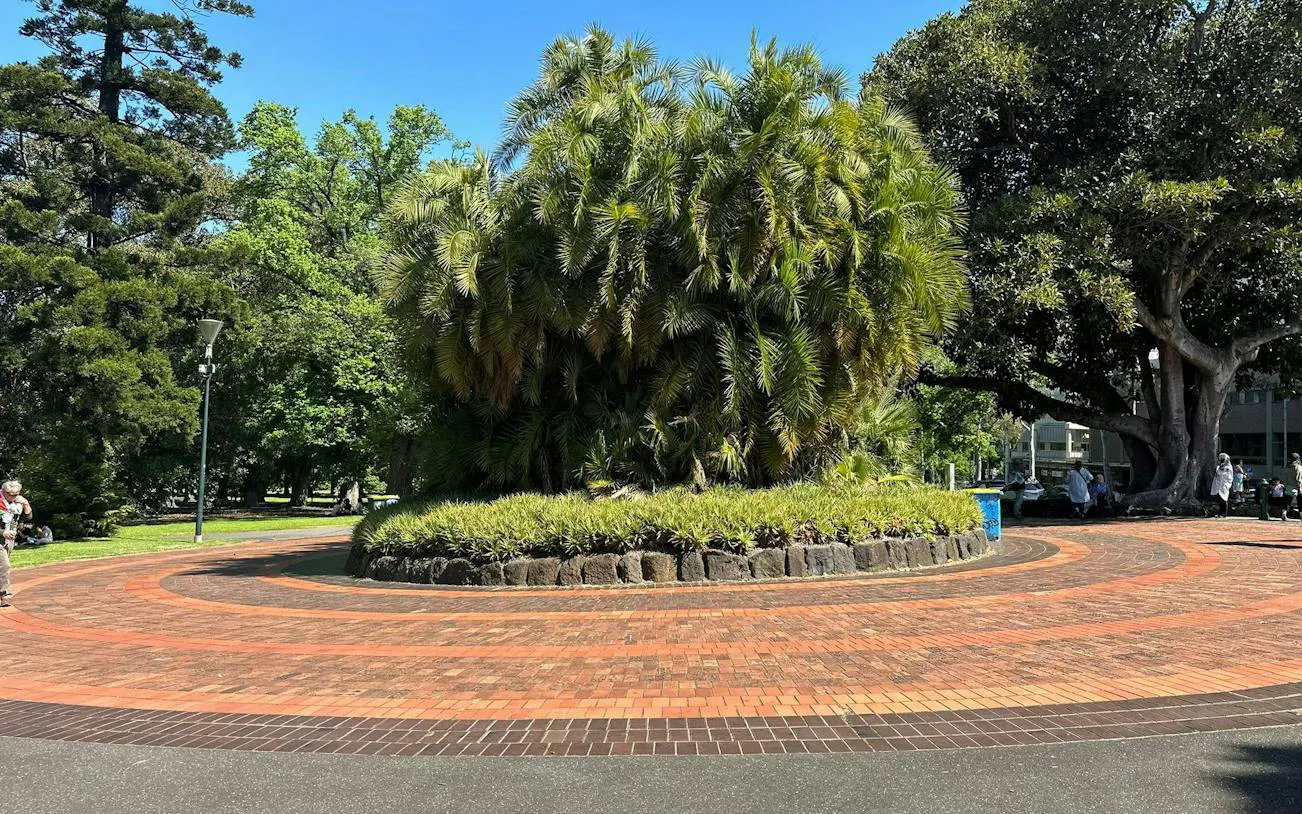 Circular brick pathway in Melbourne's Fitzroy Gardens surrounded by lush greenery.