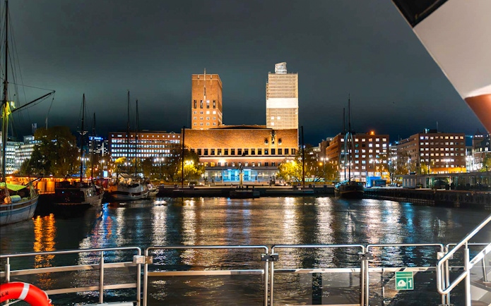 Oslo City Hall illuminated at night, viewed from a dinner cruise boat on the harbor.