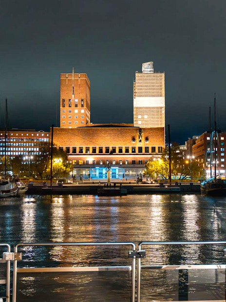 Oslo City Hall illuminated at night, viewed from a dinner cruise boat on the harbor.