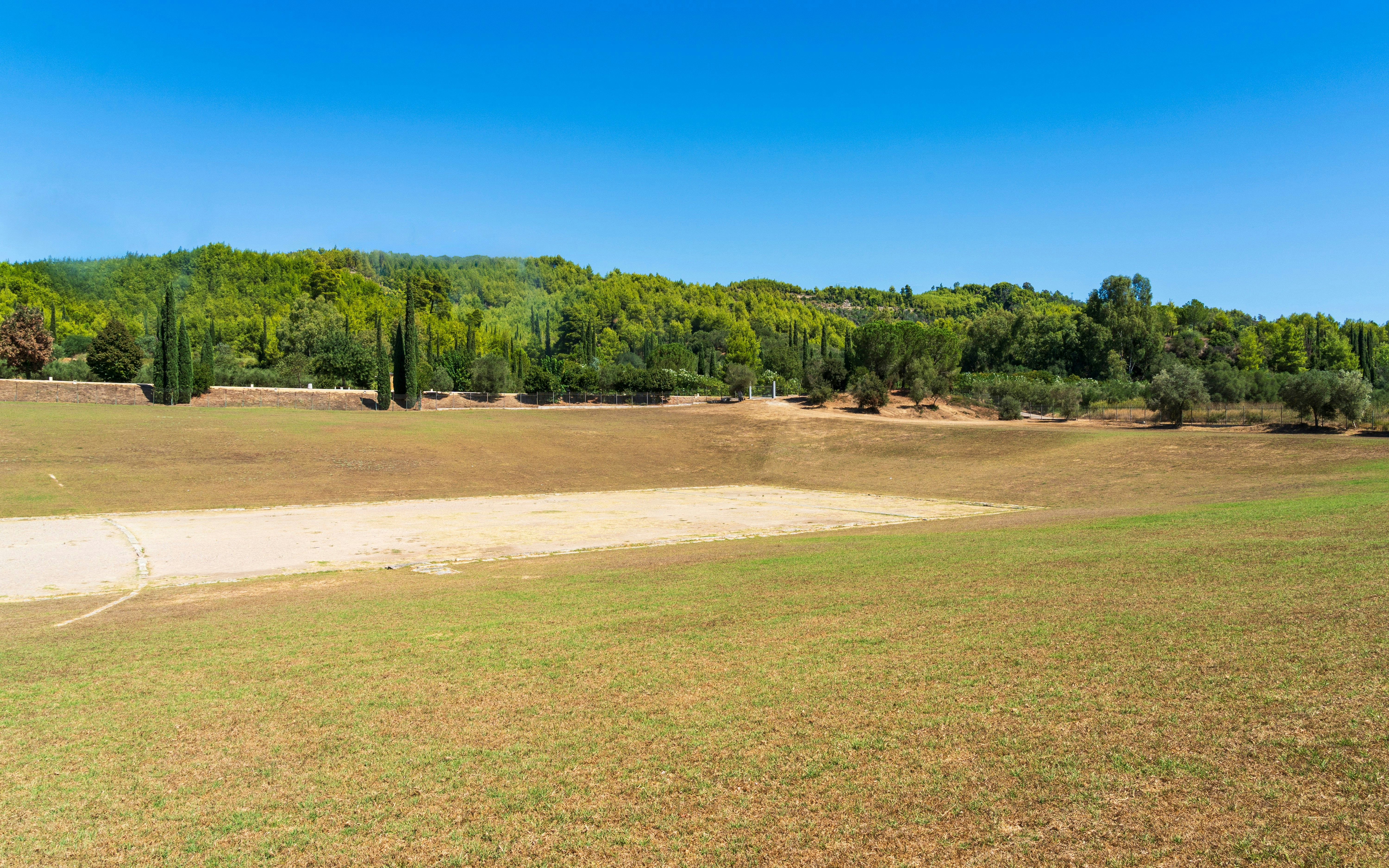 Ancient Olympic stadium field in Olympia, Greece, surrounded by greenery.
