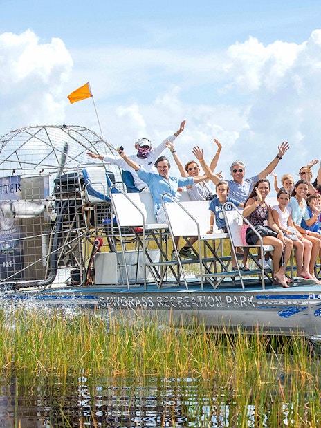 Group enjoying an airboat ride through the Everglades with grassy wetlands in the background.