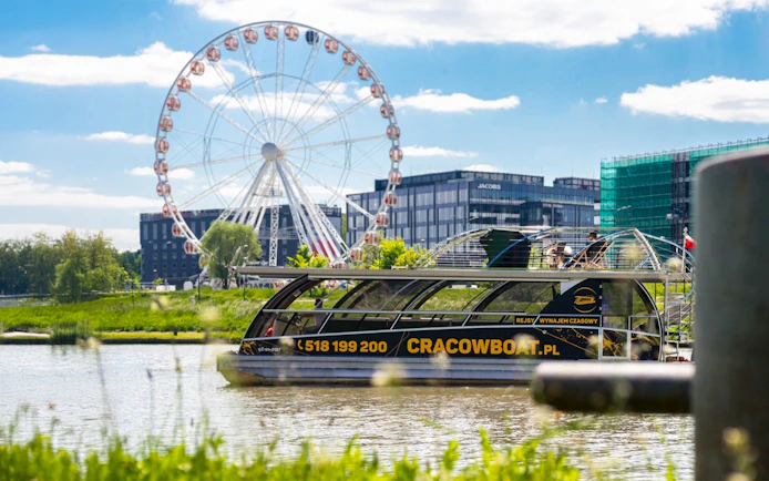 Catamaran on Vistula River with ferris wheel in Krakow background.