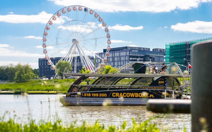 Catamaran on Vistula River with ferris wheel in Krakow background.