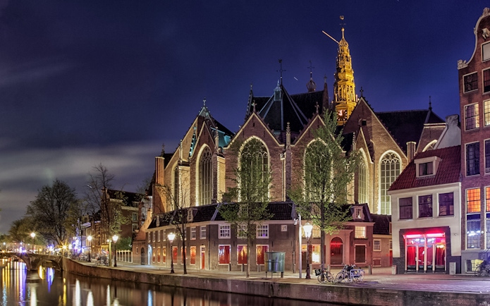 Oude Kerk exterior illuminated at night, Amsterdam canal in foreground.