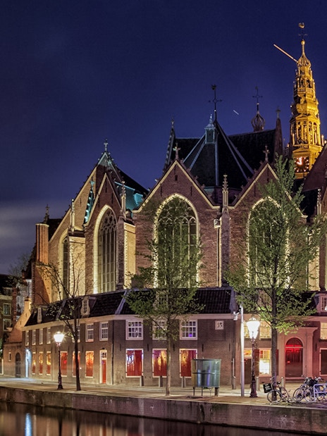 Oude Kerk exterior illuminated at night, Amsterdam canal in foreground.