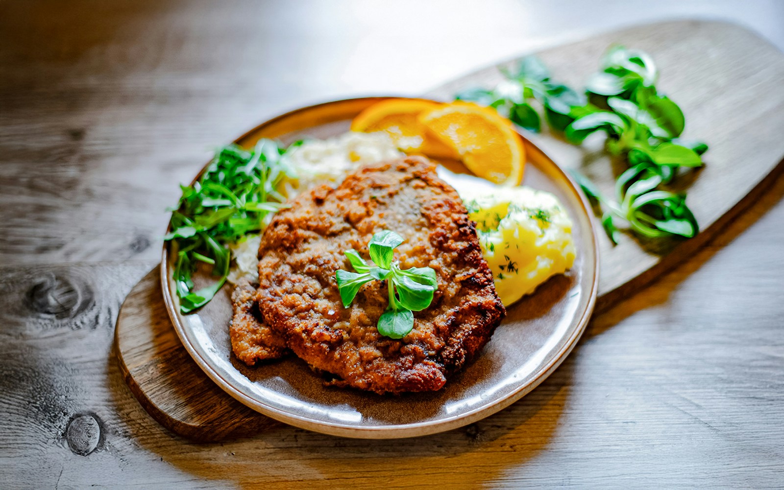 Viennese Schnitzel with mashed potatoes and greens on a wooden table.