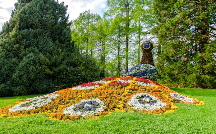 Floral peacock sculpture on Mainau Flower Island surrounded by lush greenery.