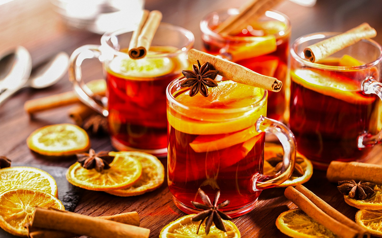 Weihnachtspunsch with cinnamon sticks and orange slices in glass mugs.