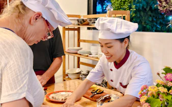 Hoi An cooking class with chef guiding participant in preparing local dish.