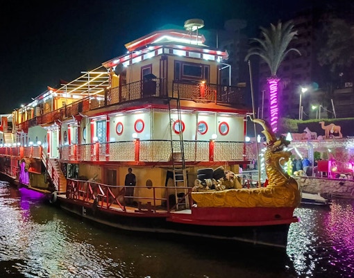 Nile dinner cruise boat illuminated at night with decorative lights and dragon figurehead.
