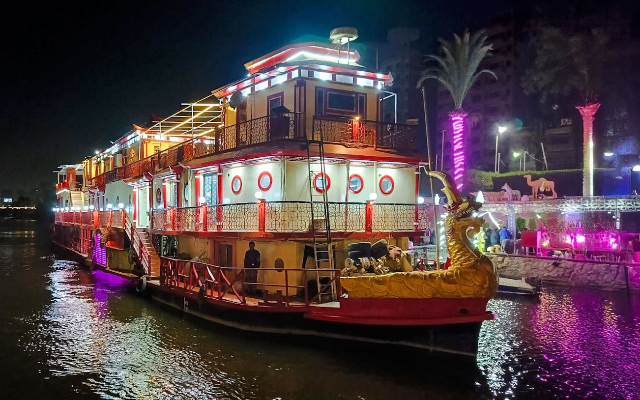Nile dinner cruise boat illuminated at night with decorative lights and dragon figurehead.