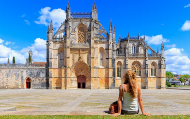 Tourist sitting outside Batalha Monastery in Portugal, admiring Gothic architecture.