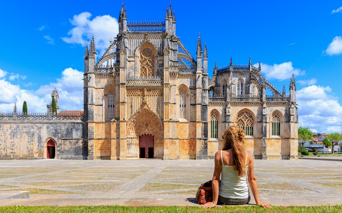 Tourist sitting outside Batalha Monastery in Portugal, admiring Gothic architecture.