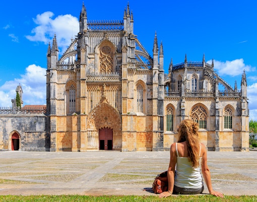 Tourist sitting outside Batalha Monastery in Portugal, admiring Gothic architecture.
