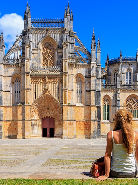 Tourist sitting outside Batalha Monastery in Portugal, admiring Gothic architecture.
