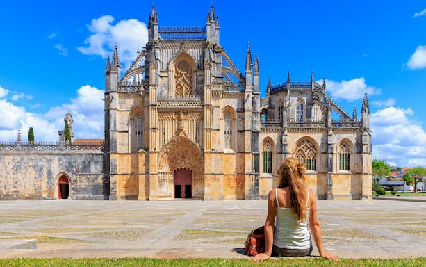 Tourist sitting outside Batalha Monastery in Portugal, admiring Gothic architecture.