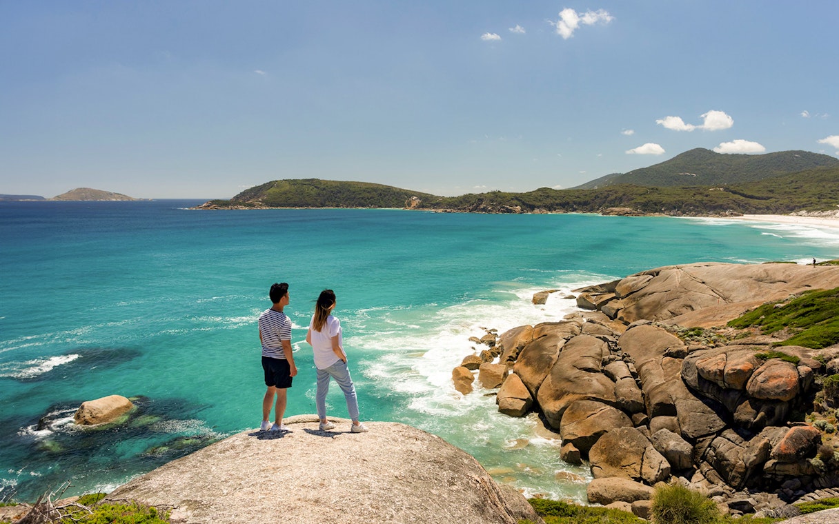 Couple overlooking turquoise waters and rocky coastline at Wilsons Promontory National Park.