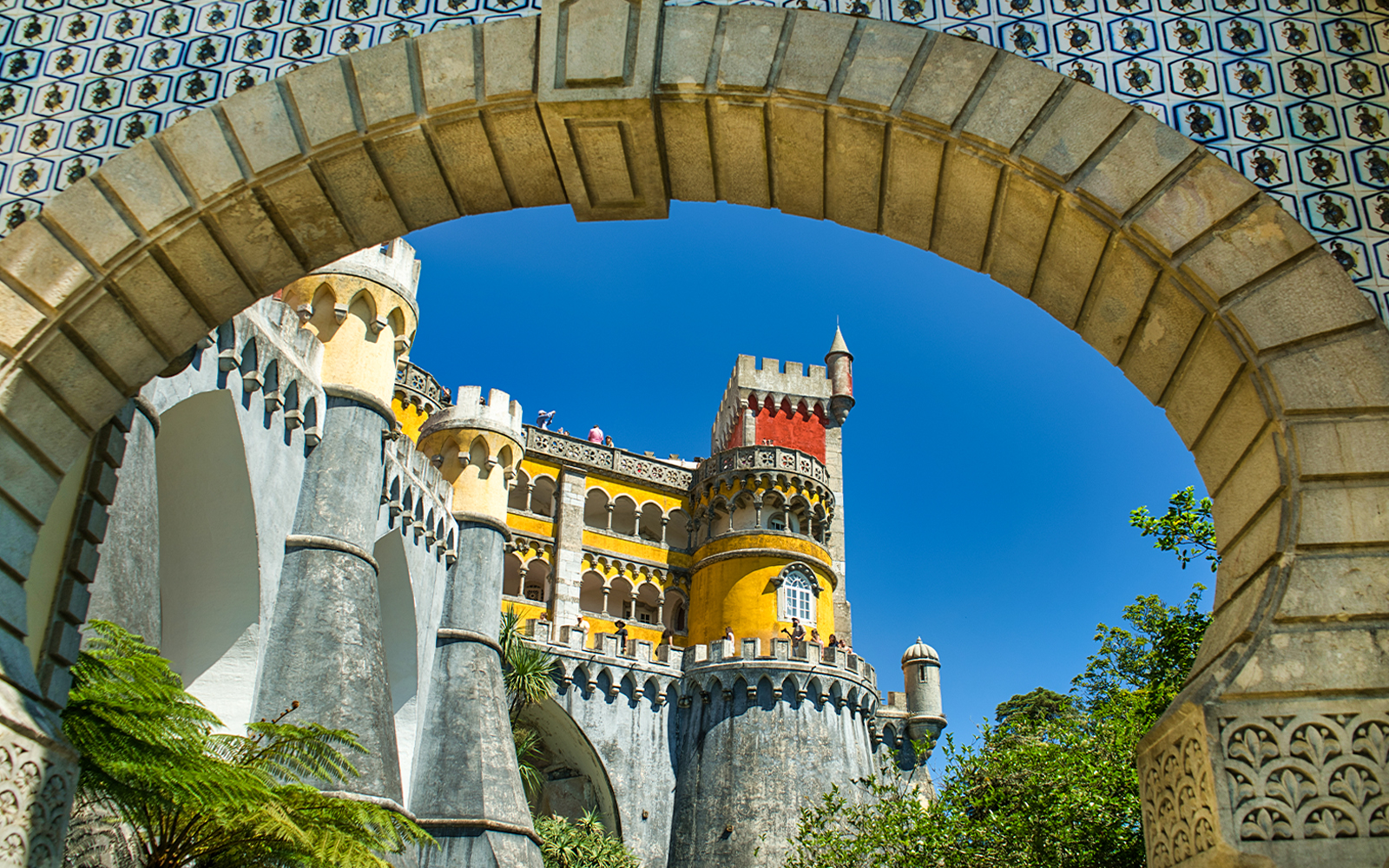 Pena Palace colorful facade viewed through stone archway, Sintra, Portugal.