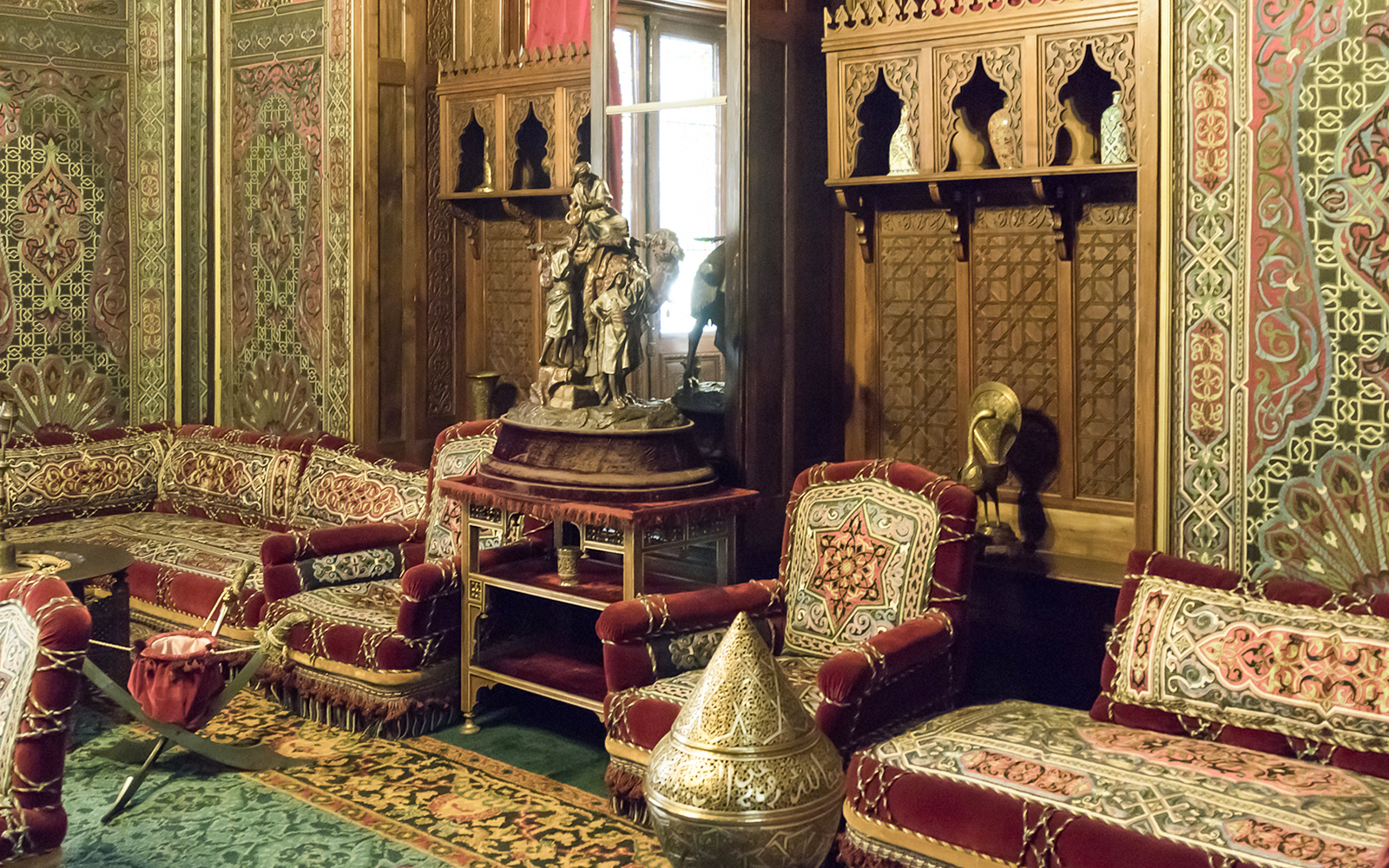 Ornate room with carved wood panels and plush red seating in Peles Castle, Sinaia.