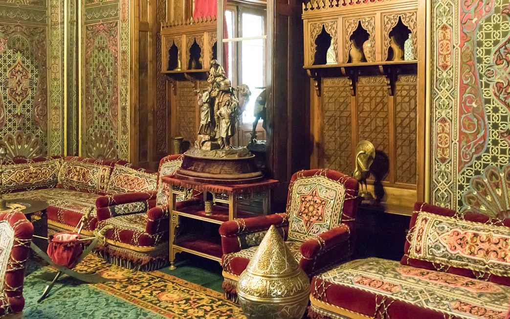 Ornate room with carved wood panels and plush red seating in Peles Castle, Sinaia.