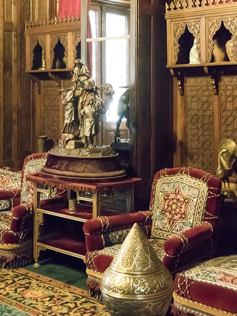 Ornate room with carved wood panels and plush red seating in Peles Castle, Sinaia.