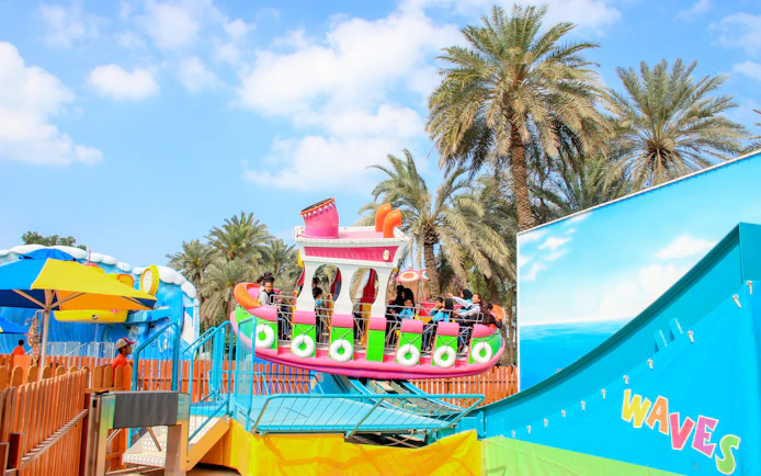 Rocking tug ride at Al Montazah Parks, Island of Legends, with palm trees in the background.