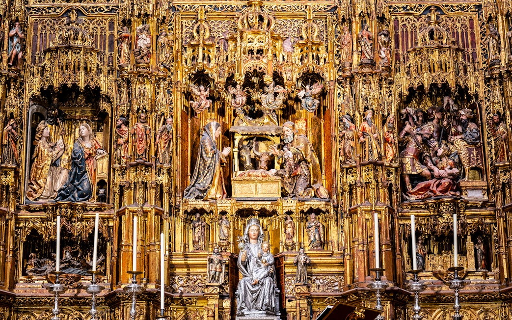 Intricate altarpiece in Seville Cathedral, featuring religious sculptures and gold detailing.