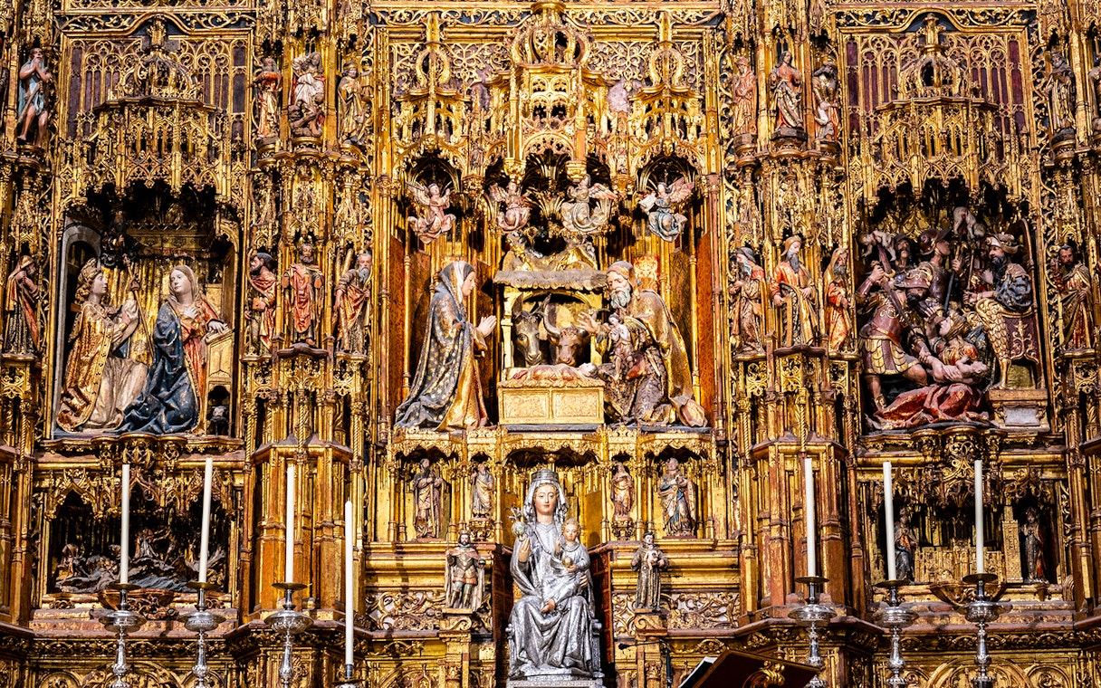 Intricate altarpiece in Seville Cathedral, featuring religious sculptures and gold detailing.
