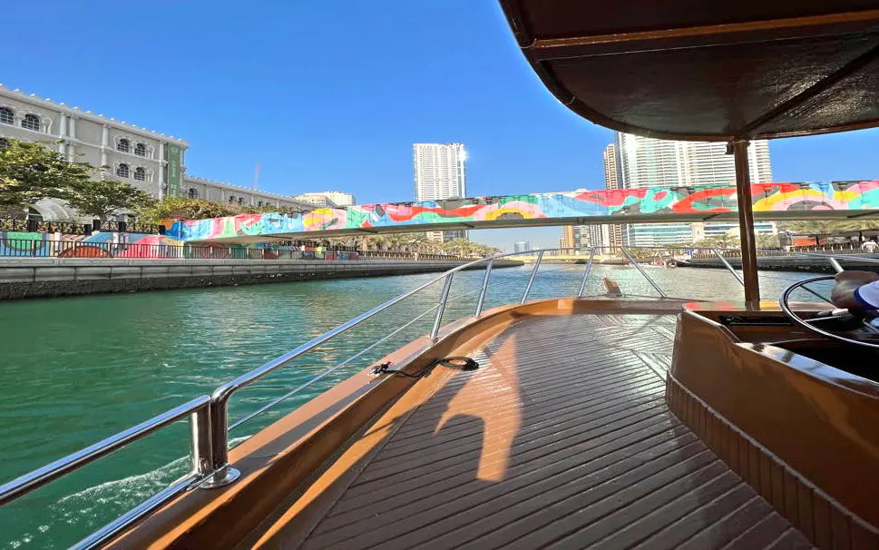 Boat cruising under colorful bridge in Sharjah canal tour.