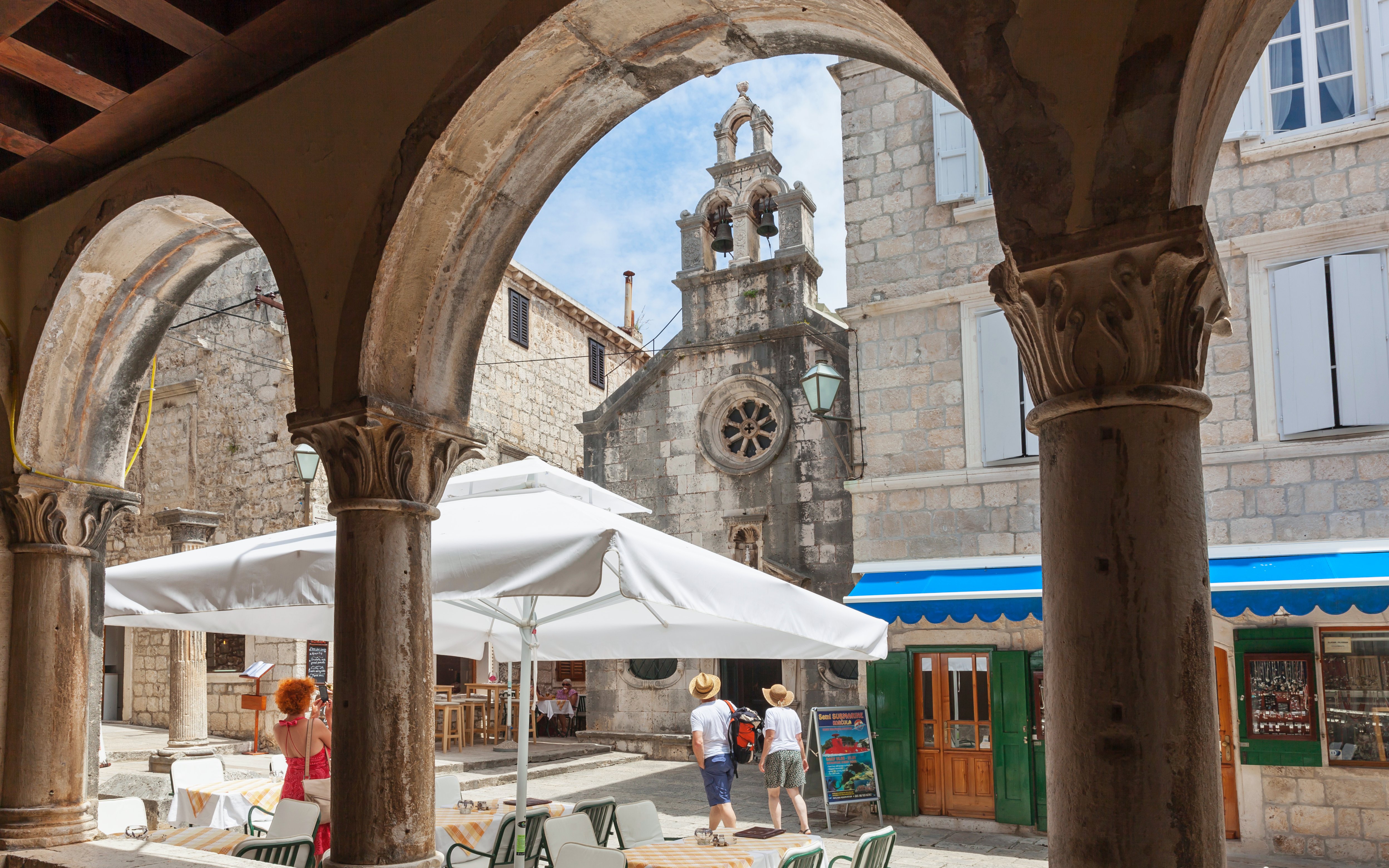 View through stone arches to a bustling square in medieval Korcula, Dalmatia, Croatia.