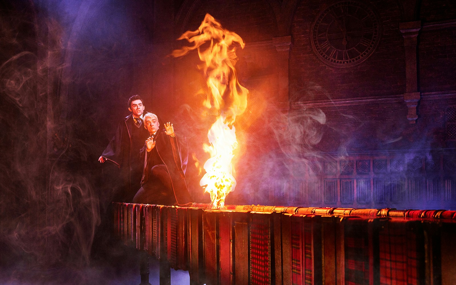 Two actors in wizard robes react to flames on stage in "Harry Potter and the Cursed Child.