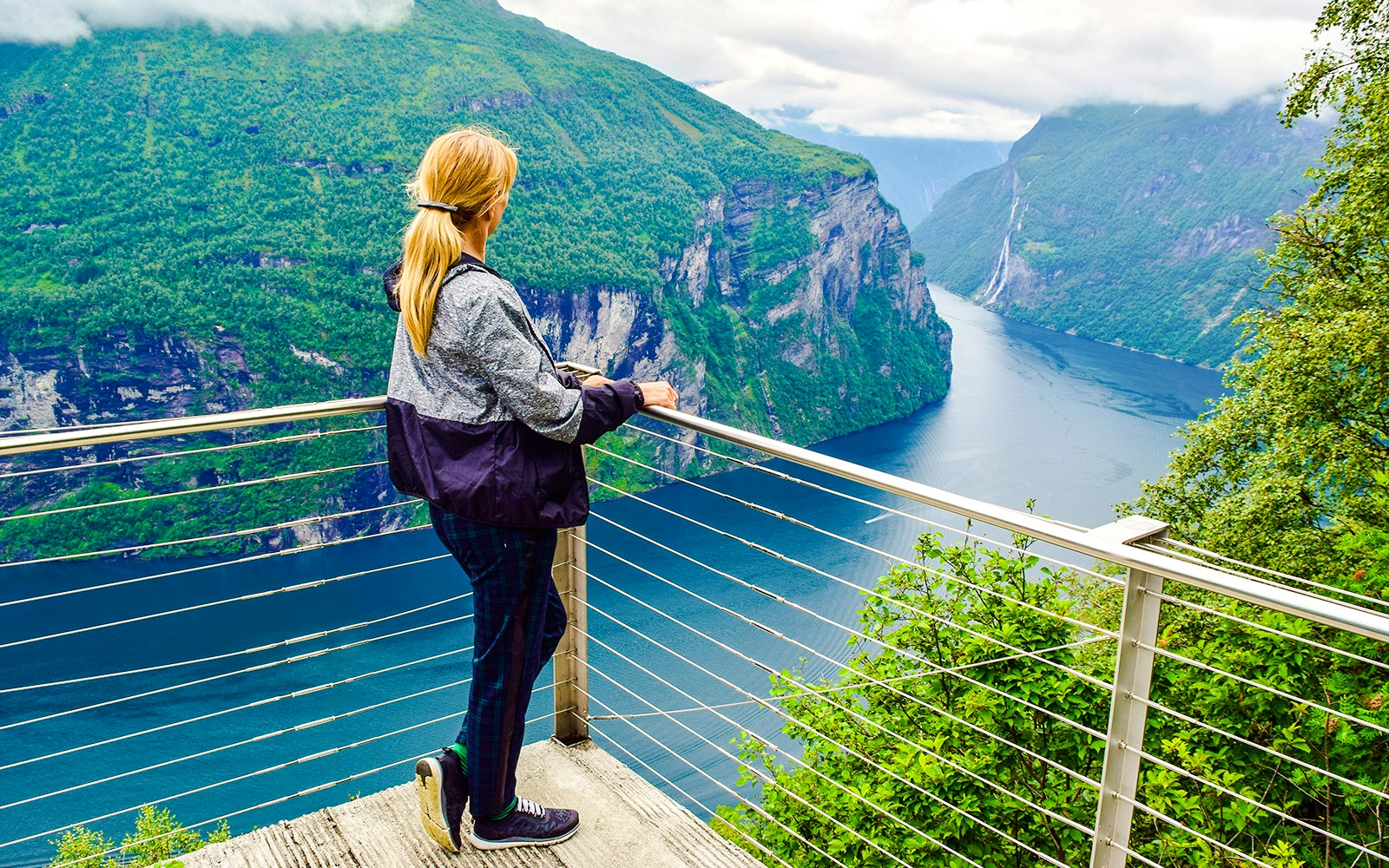 Woman at viewpoint overlooking Geirangerfjord and Seven Sisters waterfall in Norway.