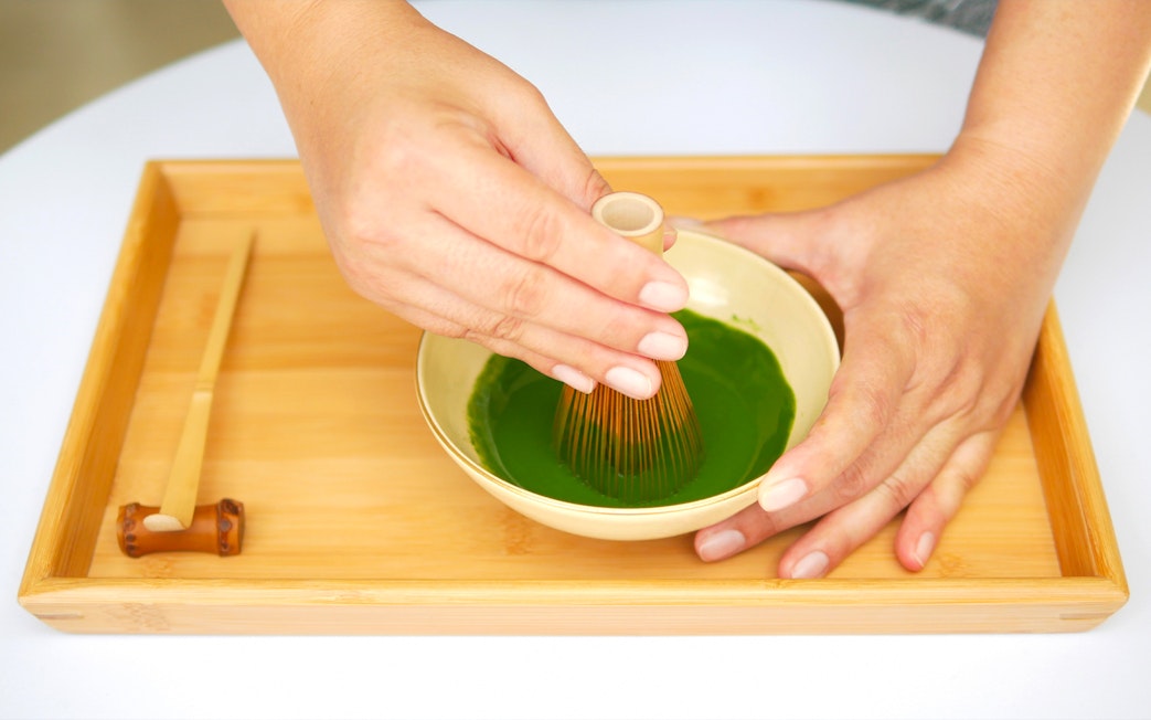 Whisking matcha in a bowl on a bamboo tray.