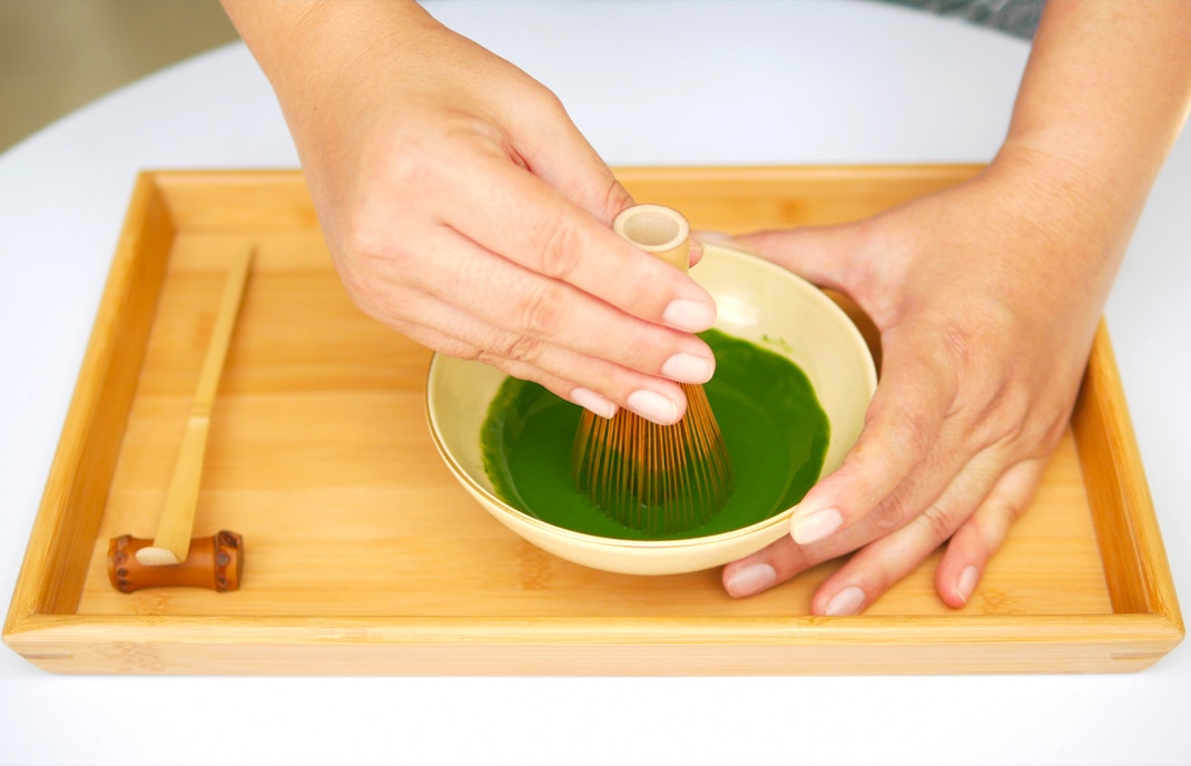 Whisking matcha in a bowl on a bamboo tray.