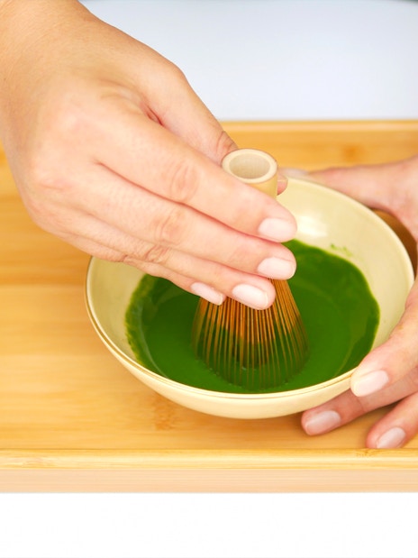 Whisking matcha in a bowl on a bamboo tray.