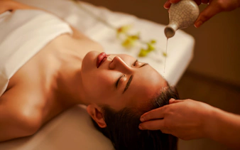 Warm oil being poured onto a person's forehead during a head massage.