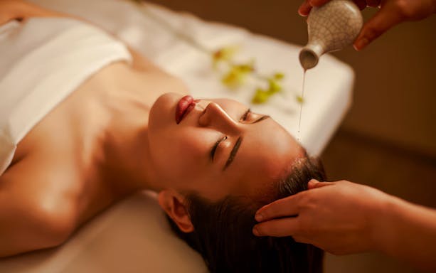 Warm oil being poured onto a person's forehead during a head massage.