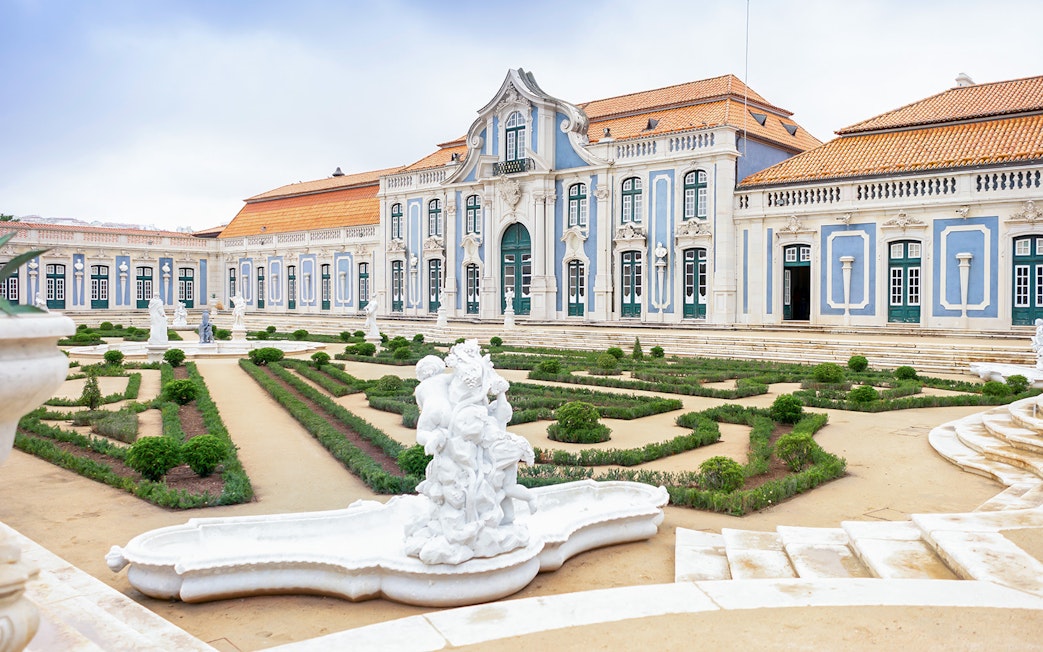 National Palace of Queluz facade with manicured gardens and statues in Lisbon, Portugal.