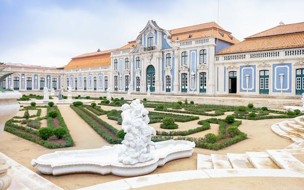 National Palace of Queluz facade with manicured gardens and statues in Lisbon, Portugal.