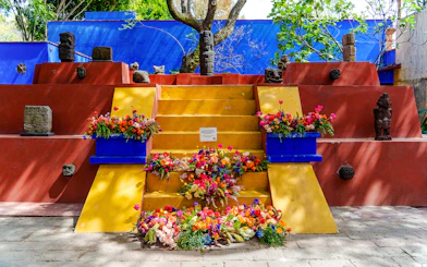 Yellow steps with colorful flowers and stone sculptures at Frida Kahlo Museum, Mexico City.