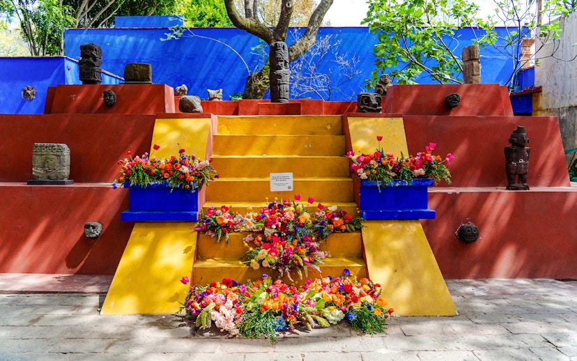 Yellow steps with colorful flowers and stone sculptures at Frida Kahlo Museum, Mexico City.