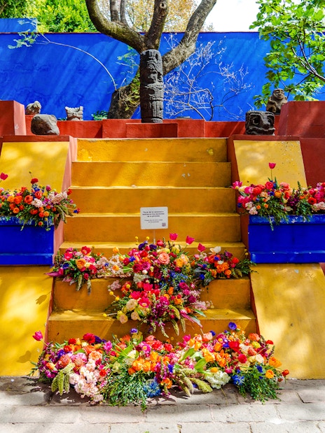 Yellow steps with colorful flowers and stone sculptures at Frida Kahlo Museum, Mexico City.