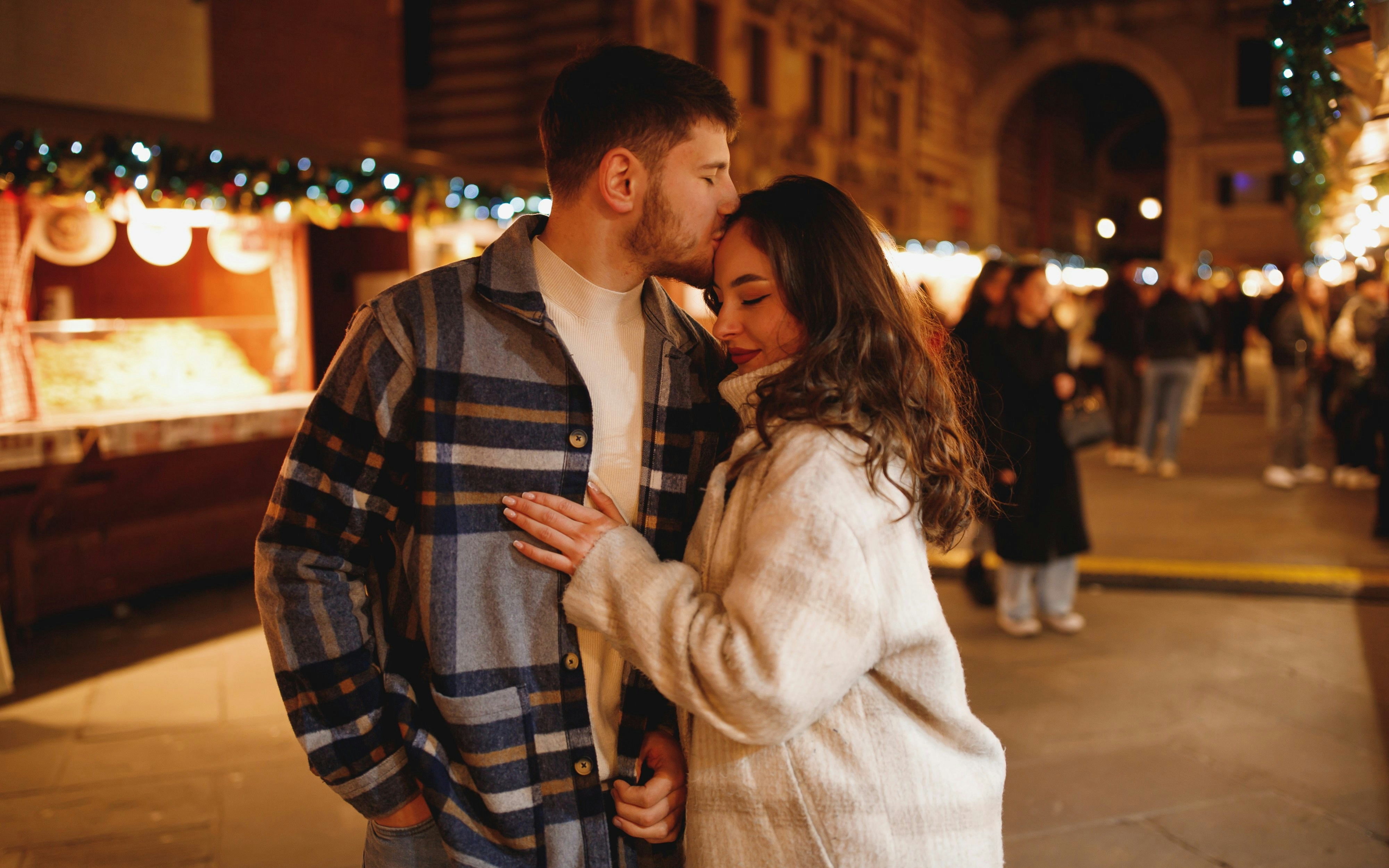Couple in checkered coats embracing at night in Verona's Piazza dei Signori.
