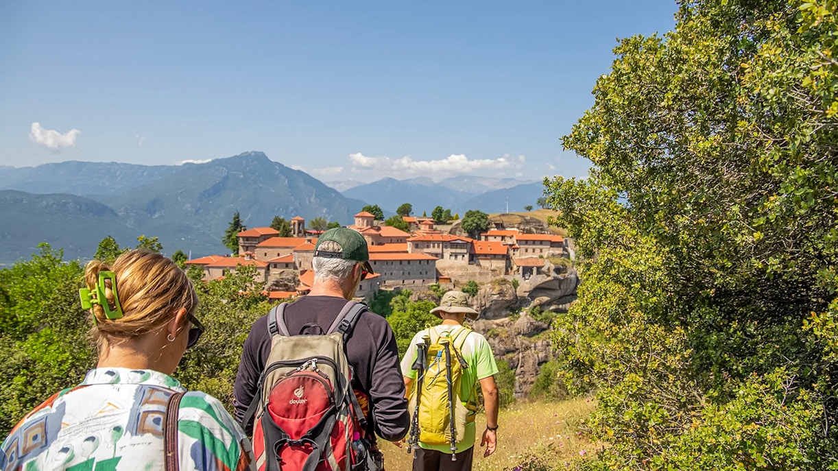 Guests hiking towards Meteora monastery with mountain backdrop.