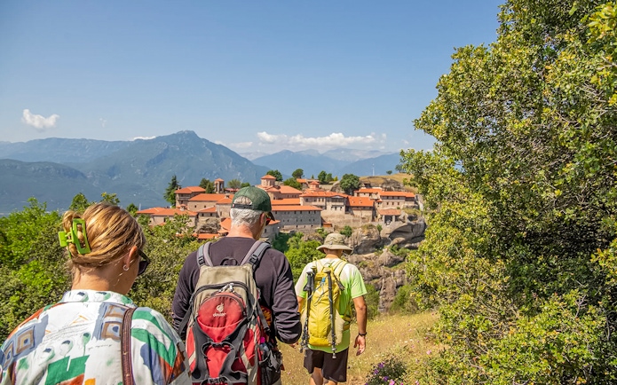 Guests hiking towards Meteora monastery with mountain backdrop.