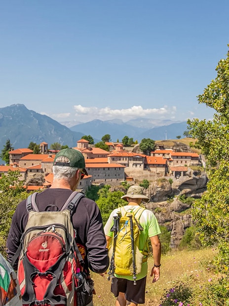 Guests hiking towards Meteora monastery with mountain backdrop.