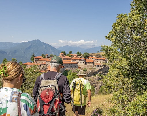 Guests hiking towards Meteora monastery with mountain backdrop.