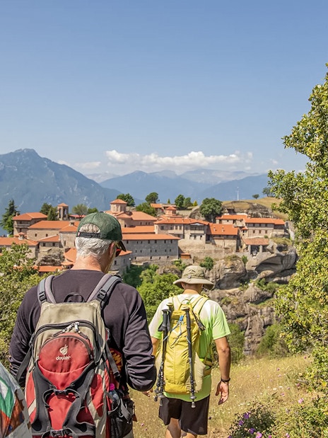 Guests hiking towards Meteora monastery with mountain backdrop.